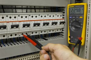 Elecwork working on BMS panel with multimeter testing voltage on an electrical panel circuit breaker